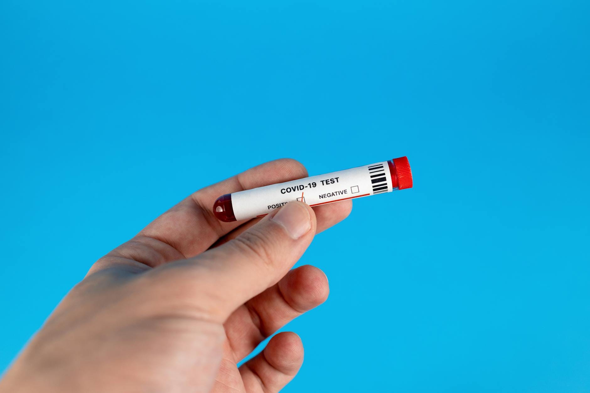 Dłoń trzymająca probówkę z testem COVID-19 na niebieskim tle