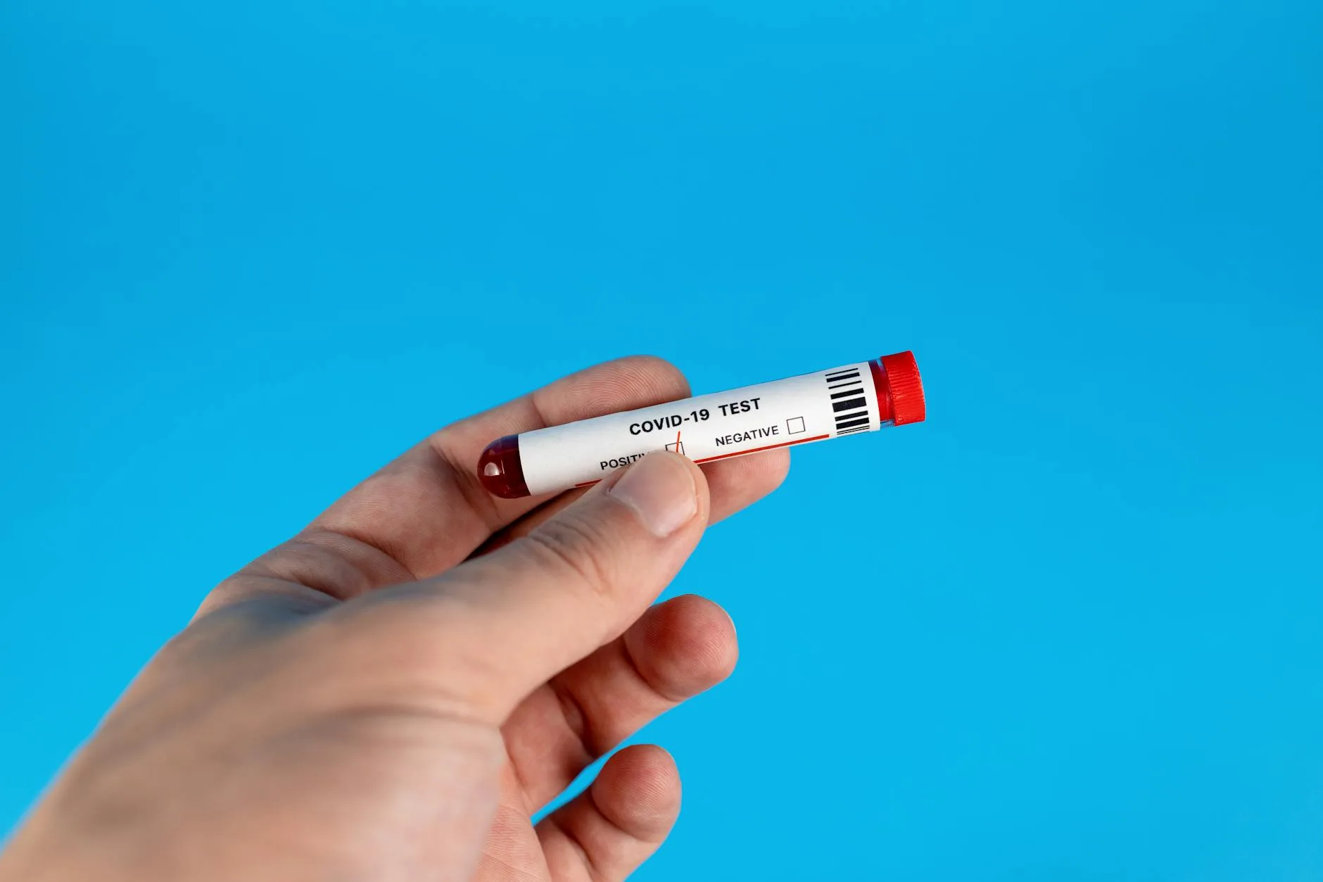 Dłoń trzymająca probówkę z testem COVID-19 na niebieskim tle