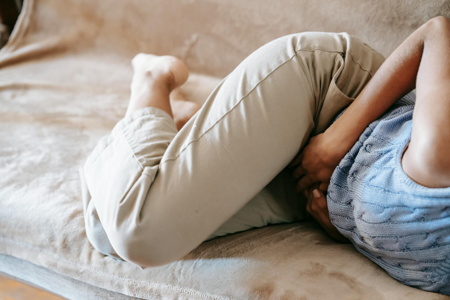 Osoba z bólem brzucha leżąca na kanapie w domu