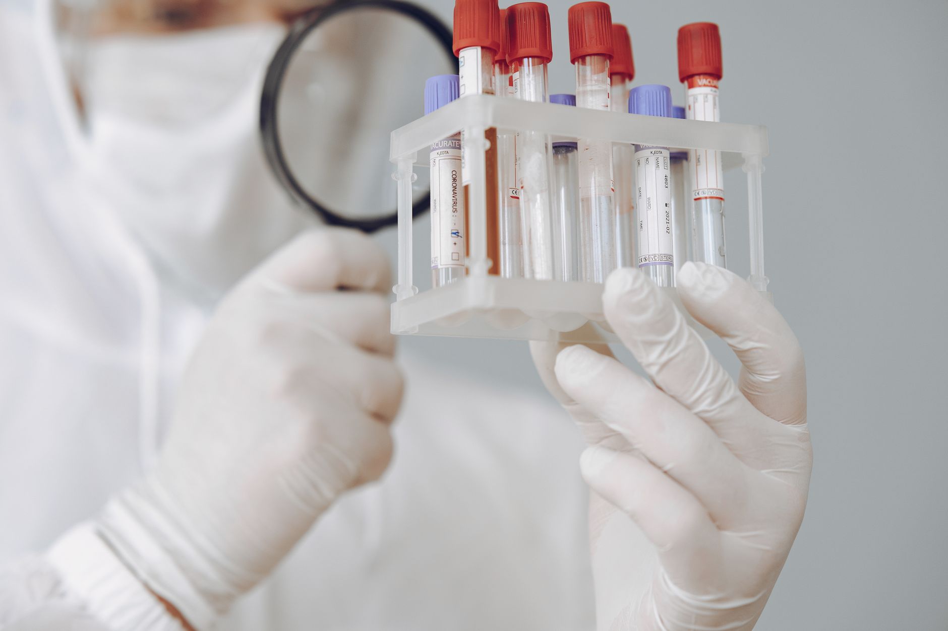 Laborant w ochronnym stroju analizuje próbki krwi pod lupą